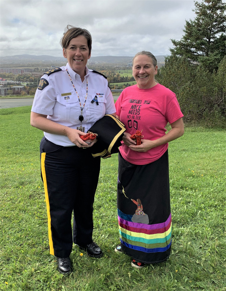 Une femme vêtue de l'uniforme de commandante divisionnaire de la GRC se tient à côté d'une femme autochtone. Elles tiennent toutes deux des cadeaux de remerciement. À partir de la gauche : la commandante divisionnaire de la GRC à T.N.L. Jennifer Ebert et Arlene Blanchard White 