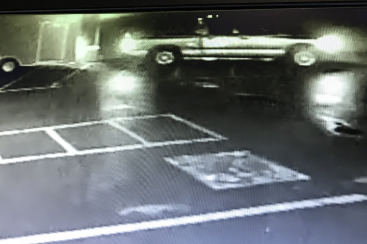 A black and white surveillance photo is obtained showing a pickup truck towing an enclosed utility trailer across a paved parking lot at night.