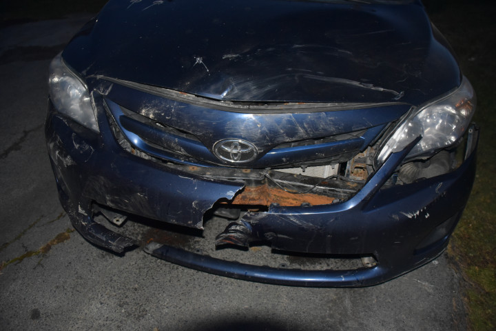 The front bumper of a blue Toyota vehicle is pictured, heavily damaged. 