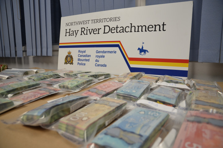 Seized cash, sorted and bagged, on a table. A sign reads Northwest Territories, Hay River Detachment, Royal Canadian Mounted Police.