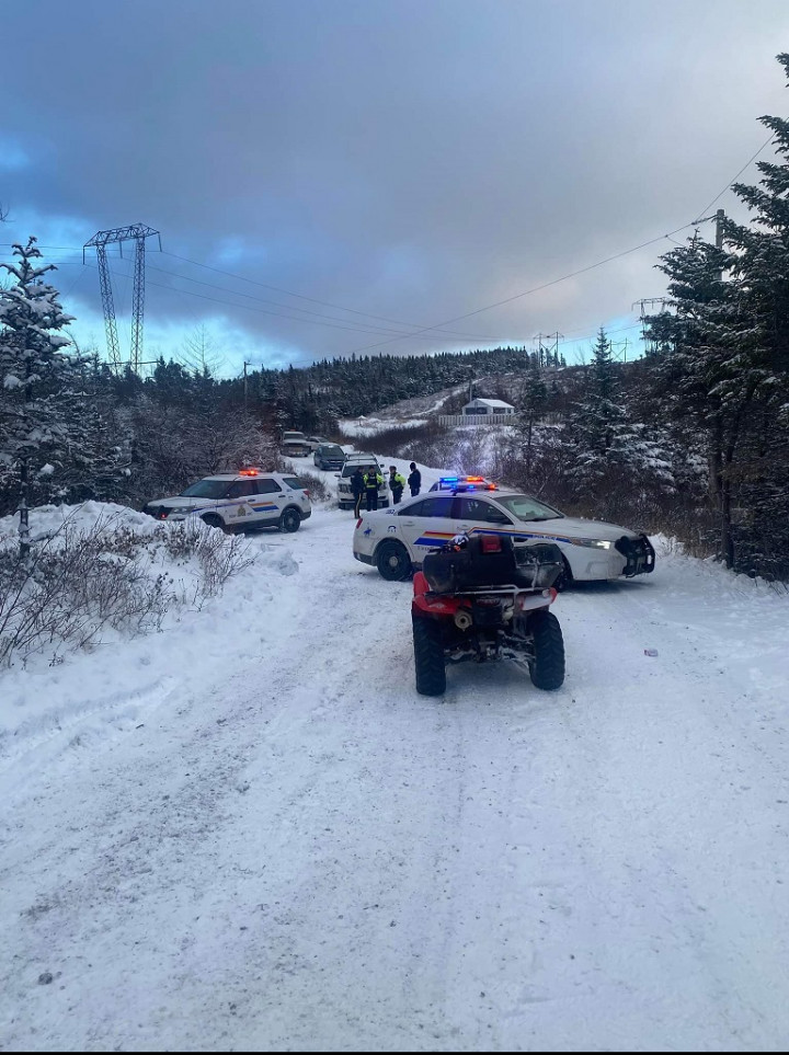 A red quad is pictured on a snow covered cabin road during the daytime. A marked RCMP police cruiser is blocking its path with another marked police car nearby.