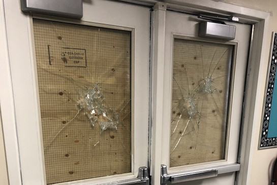 A picture of a double set of doors. The upper glass window pane of each door is smashed.