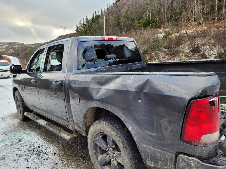 A dark blue truck is shown with windows smashed and the side panels severely damaged. 