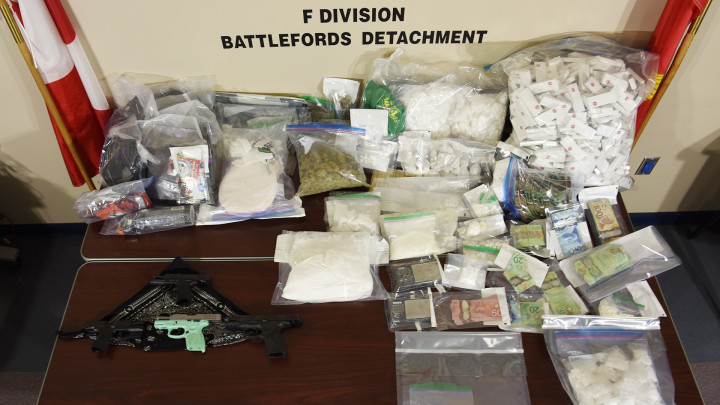 Une arme de poing, des drogues illicites et de l'argent dans des sacs de preuves en plastique sur une table.
