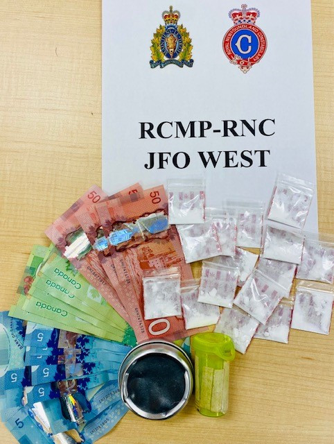 Affiche comportant le texte « RCMP-RNC JFO WEST » avec une importante quantité d'argent comptant, une bouteille de comprimés et de nombreux petits sachets de cocaïne.