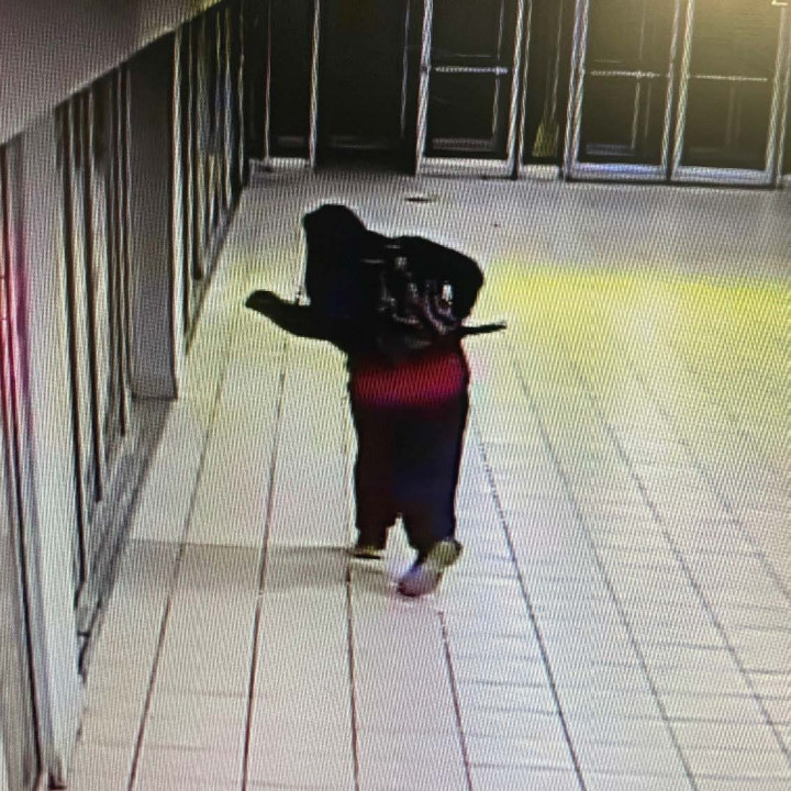 A person wearing dark clothing can be seen from behind, walking.