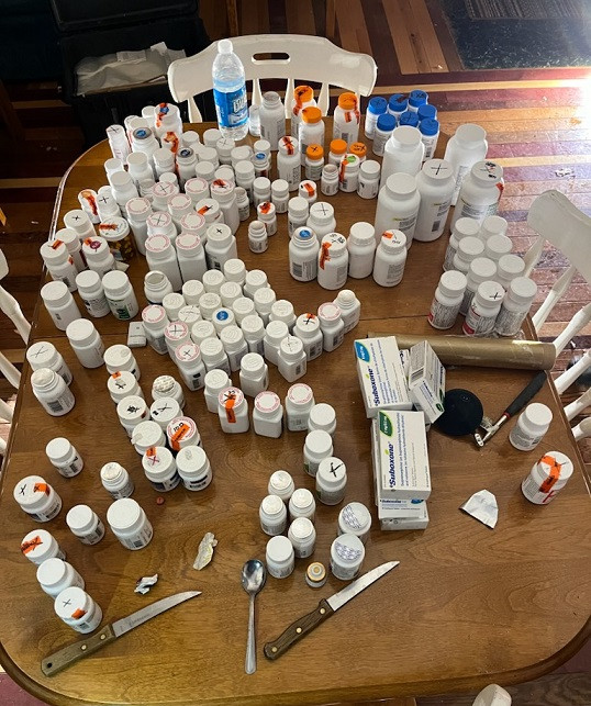 Numerous bottles of prescription narcotic medications is displayed on a wooden table.