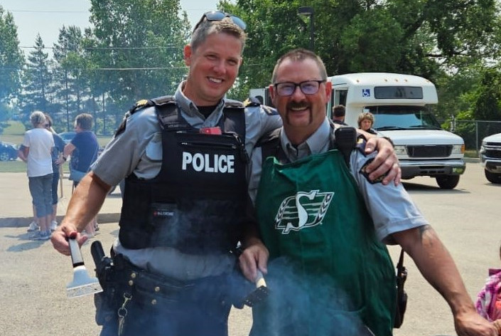 Two officers in uniform standing in front of a BBQ.