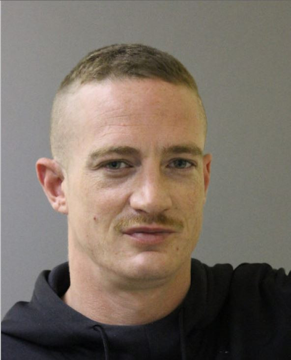 A photo of a man with light eyes, short hair which is shaved on the sides and a moustache is shown. 