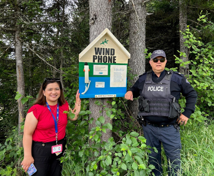 A uniformed police officer and woman stand next to a 'Wind Phone'.
