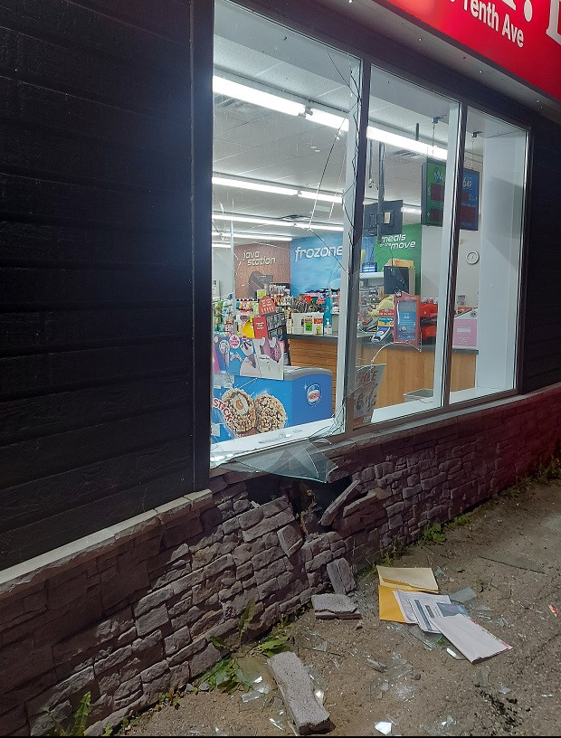 The front of a convenience store is pictured at night with damage to the window glass and brick wall.