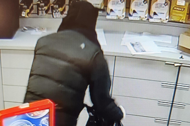 The back view of someone taking things from behind a counter at a store. 