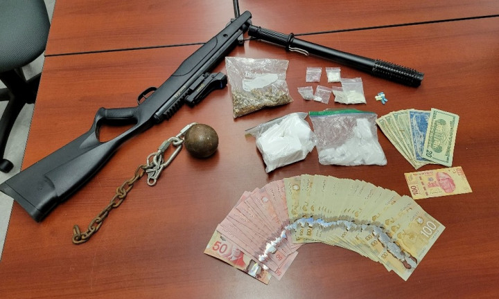 Items seized by police, including a quantity of cash, drugs in pill and powder form, an airsoft rifle, a conducted energy weapon and a ball and chain are pictured arranged on a table.