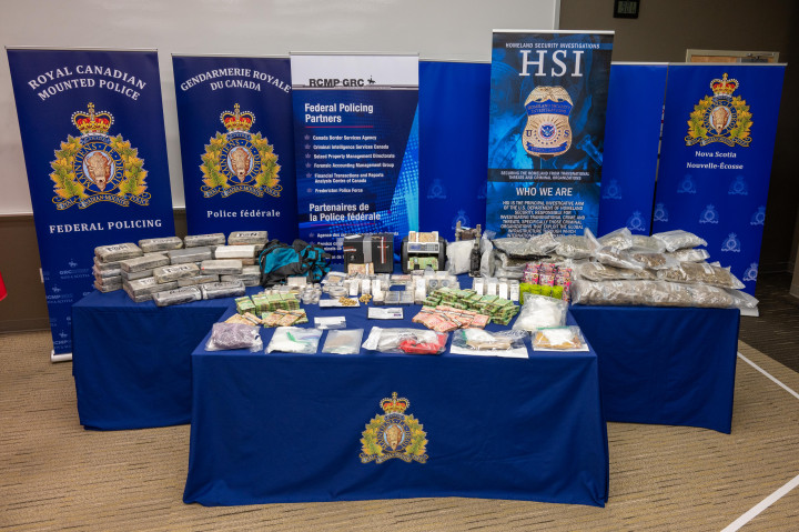 Items seized, including cash, silver bars, cocaine, displayed on a table with RCMP and Homeland Security banners in the backdrop