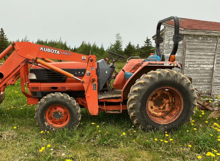 An orange Kubota farm tractor is parked on the grass.