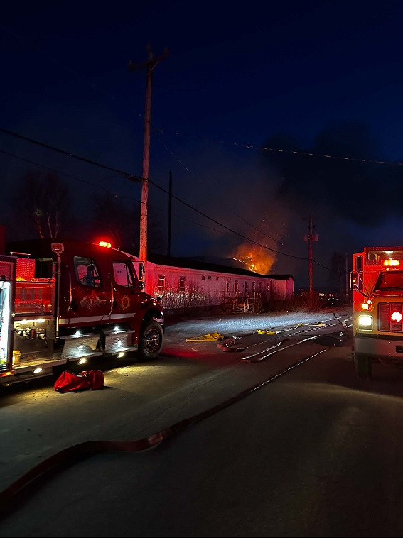 Two fire trucks are pictured near a burning building at night.