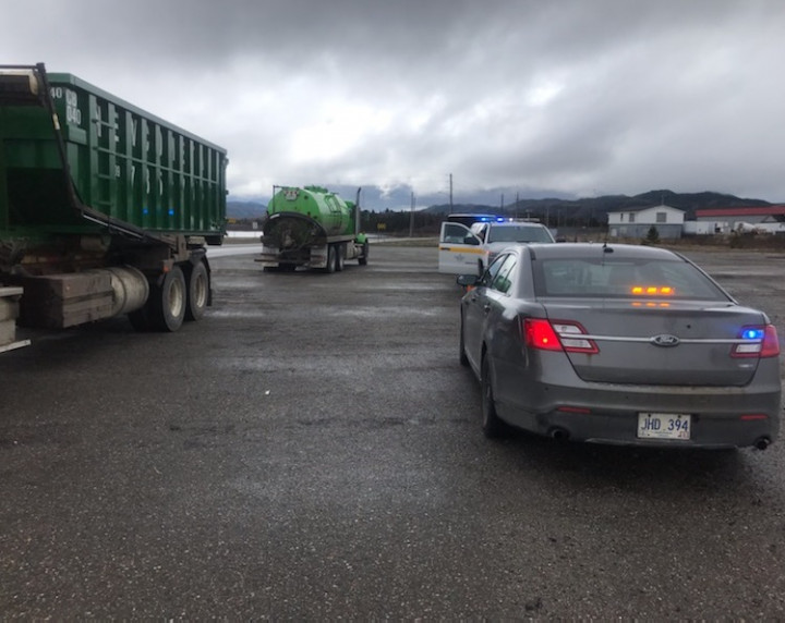 An unmarked police vehicle and a Highway Enforcement vehicle is parked beside two commercial vehicles.