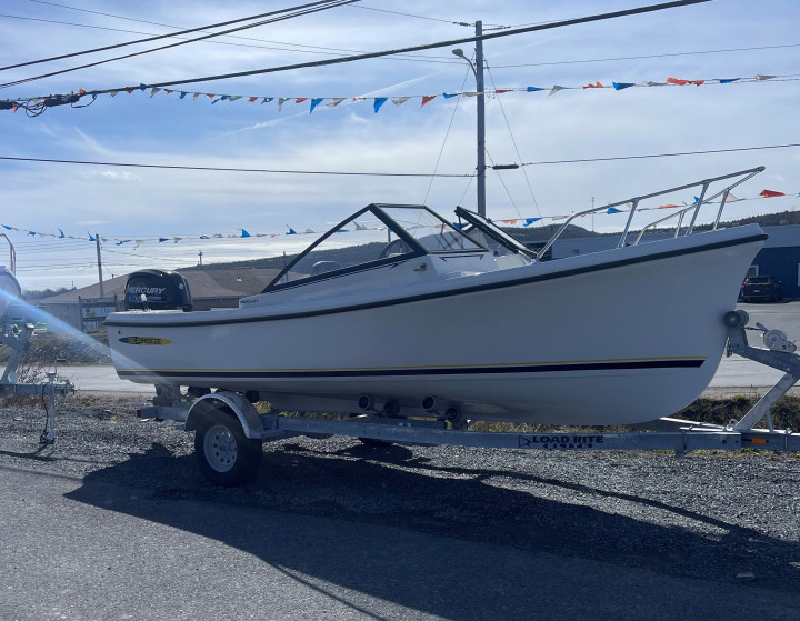 A white Seabreeze boat sits on a trailer in the parking lot of a business.