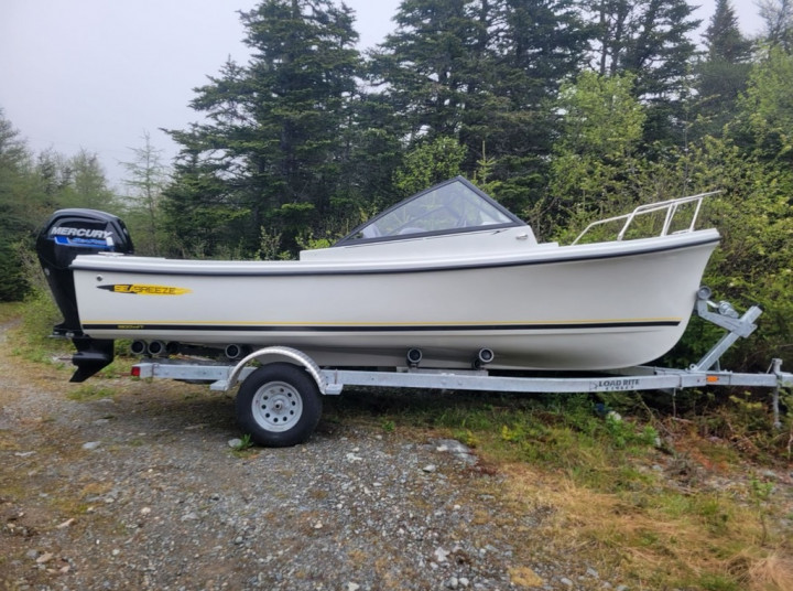 A white Seabreeze boat sits on a trailer in on a section of gravel.