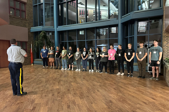 A police officer is facing a group of students who are standing in front of a big window inside a building. 