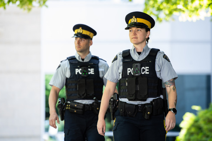 Two uniformed RCMP officers are pictured outside. Body-worn cameras are on their vests with green lights displayed.