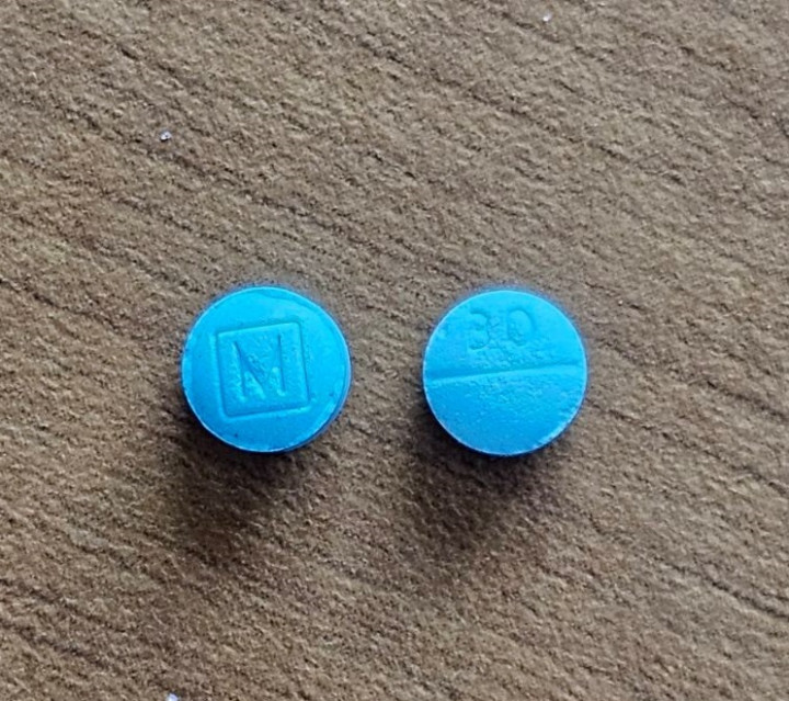 Two round blue pills are displayed. One is etched with the letter 