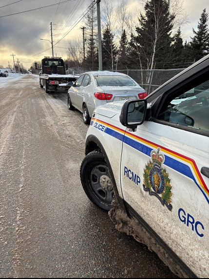 A marked RCMP vehicle is parked on the side of a roadway. A tow truck and car and parked in front of the police vehicle.