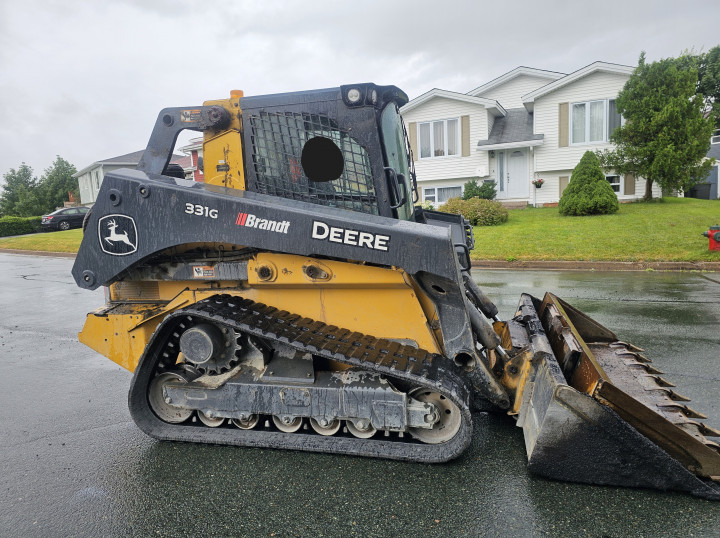 A yellow John Deere skid-steer loader on a residential street.