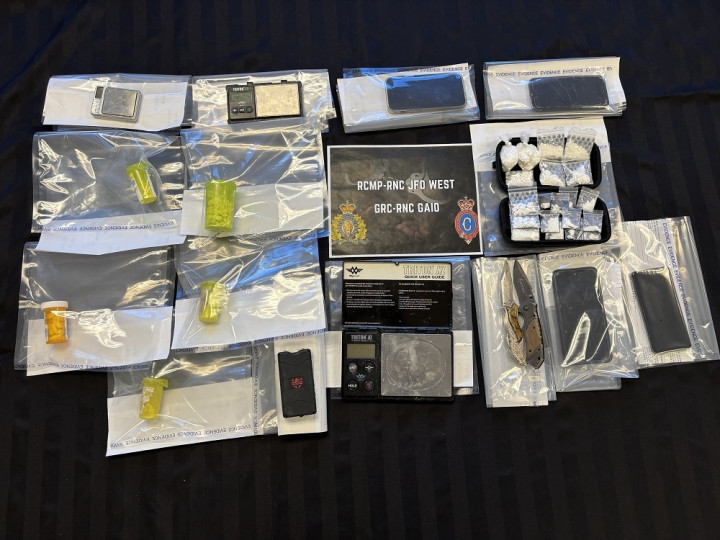 A number of items, including quantities of cocaine, prescription pills, a stun gun, knives and other items consistent with drug-trafficking, are displayed around a sign that says 