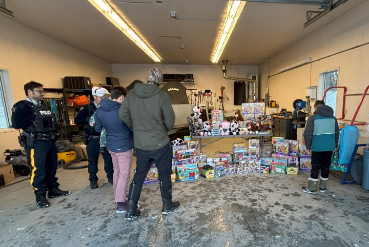 Two RCMP officers watch 3 youth who are selecting a toy from a large stack of toys.