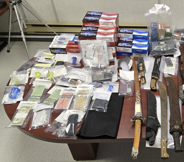 A number of items, including six knives, contraband tobacco, cash and drugs, are displayed on a table.