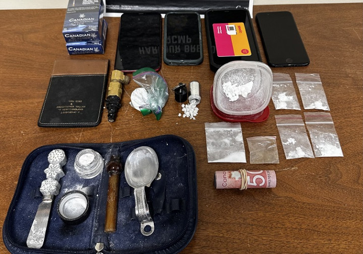 A number of items are displayed on a table, including quantities of drugs, cash, cell phones, contraband cigarettes and drug paraphernalia.