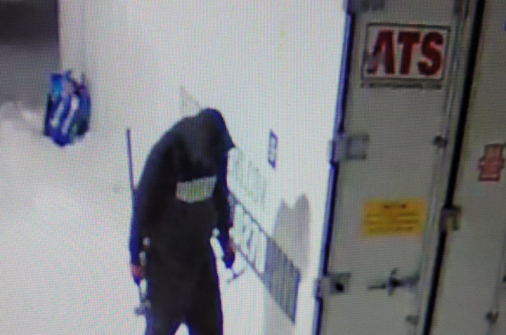 Security camera footage of a suspect wearing dark clothing and a hoodie with white lettering.