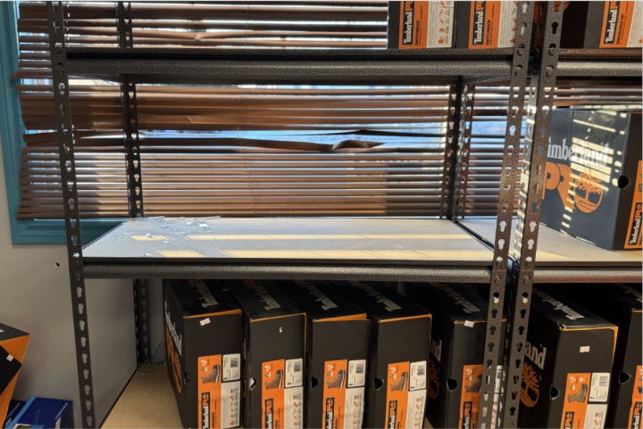 An empty shelf with broken glass. The shelves surrounding have boxes of Timberland boots. 