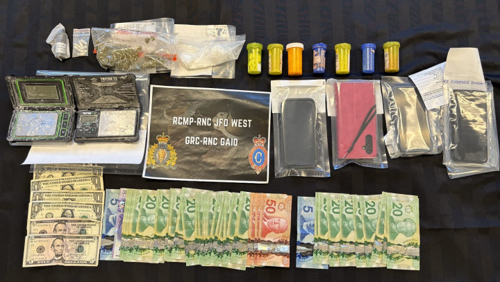 Un certain nombre d'objets sont exposés sur une table, notamment de la cocaïne, du cannabis, divers flacons de pilules, de l'argent canadien et américain, des téléphones portables et des balances numériques. Un morceau de papier sur la table indique GRC-RNC JFO West, GRN-RNC GAIO.