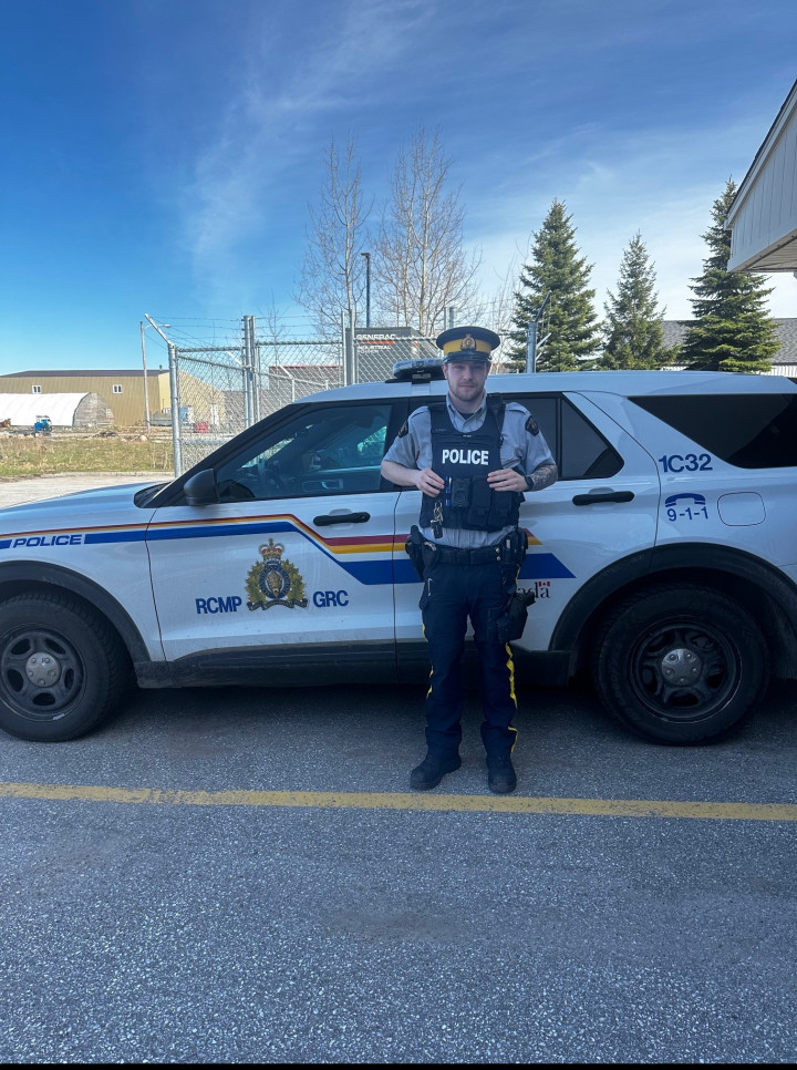 A photo of Aidan Payne in his RCMP uniform in front of a police vehicle.
