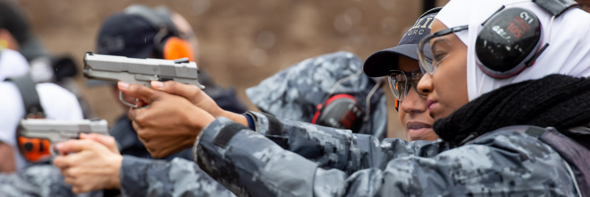 Une femme pointe une arme à feu lors d'une formation, dans un champ de tir.