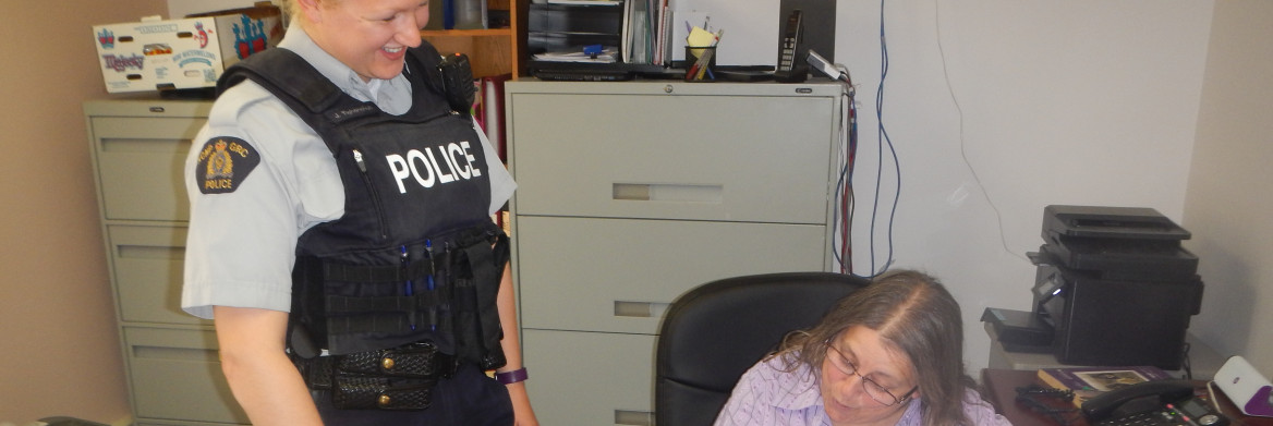 RCMP officer speaks with a woman sitting at a desk. 