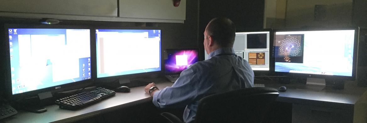 A man is seated in front of several computer screens.