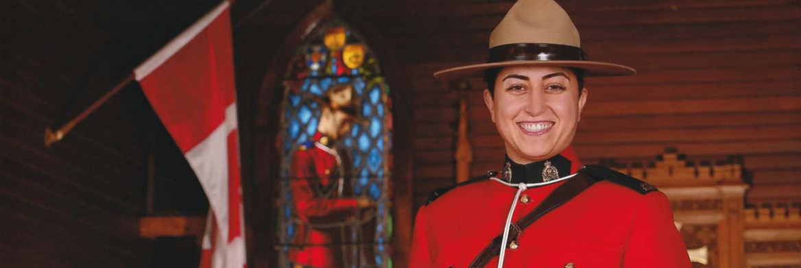 A female RCMP officer in red serge shakes the hand of a male police officer. There is a Canadian flag in the background.