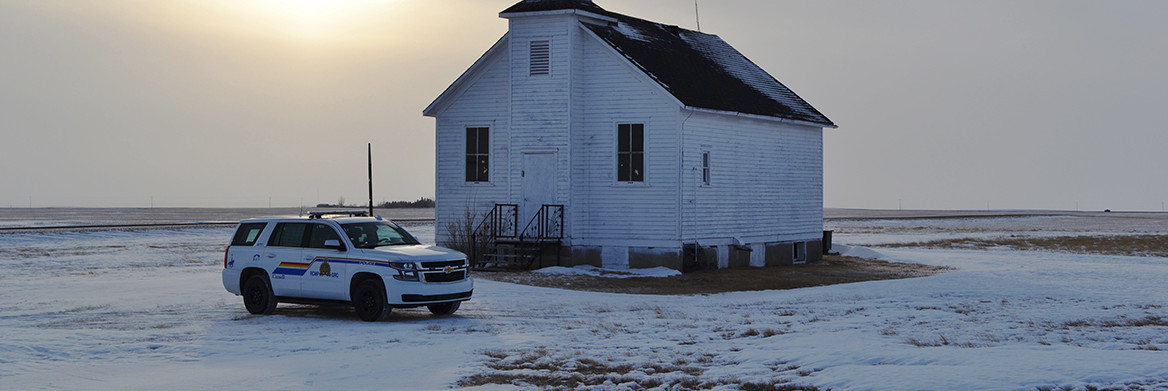 An SUV police cruiser is parked in front of a small white church surrounded by a flat snowy landscape.