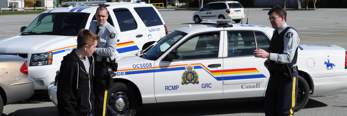 Two male RCMP officers approach a young man in a parking lot. 