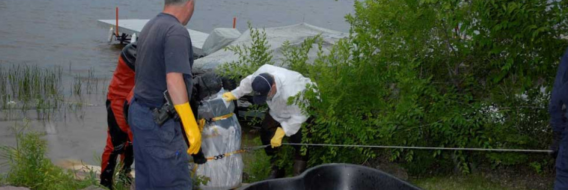 RCMP officers help steady a barrel using a cable, with a pond liner also visible.