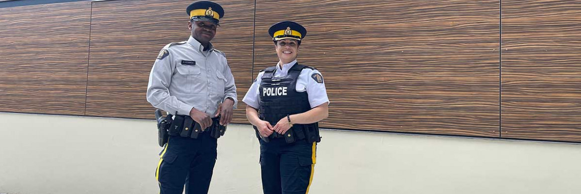 A male and female RCMP officer standing with RCMP and GRC written on the background wall.