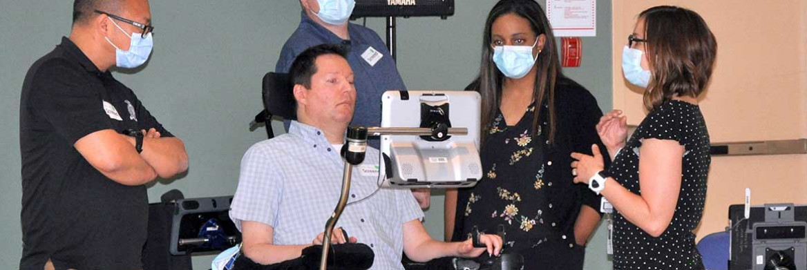 A man using a wheelchair faces a computer screen while two men and two women look at him and the screen.