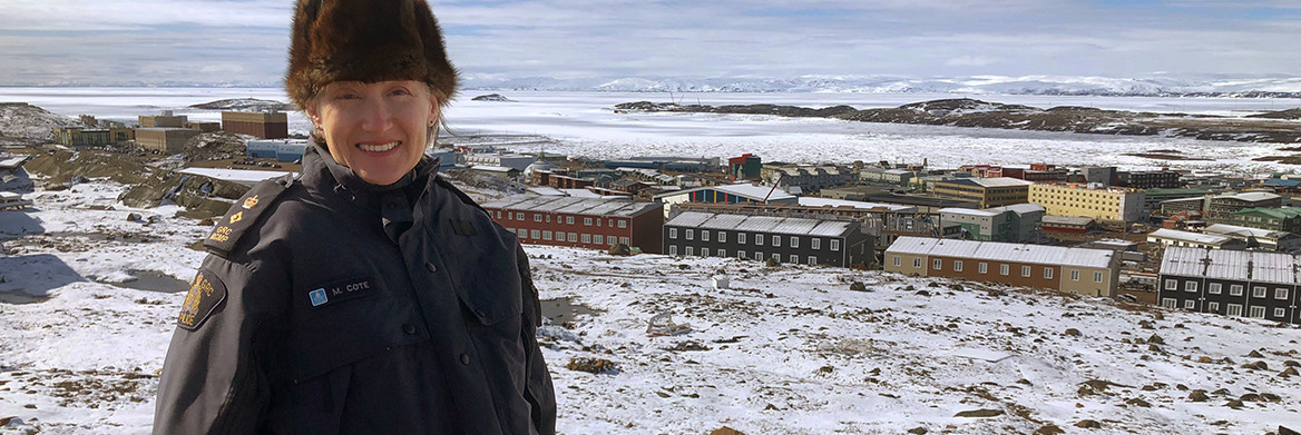 Officière de la GRC fixant la caméra avec en arrière-plan un village couvert de neige.