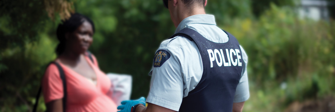 Dans une région forestière, un policier parle avec une femme enceinte chargée de sacs.