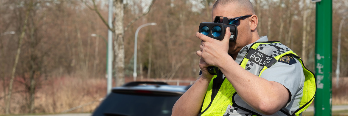 Un policier sur une route utilisant un cinémomètre laser.