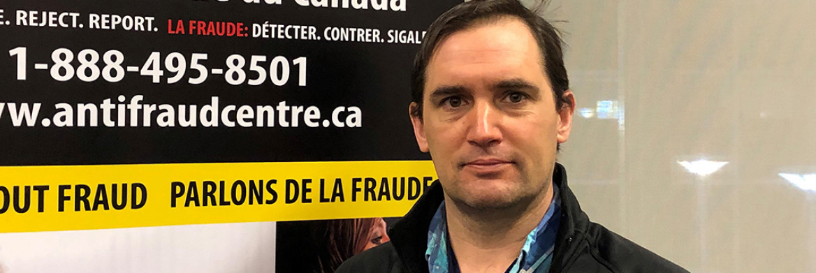 Un homme se tient à côté d'un panneau du Centre antifraude du Canada.