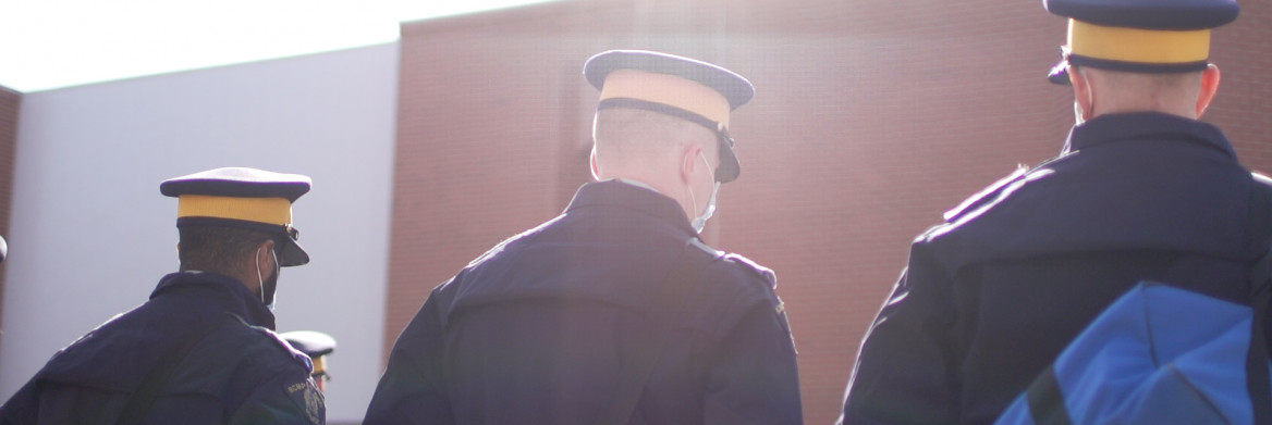 Three RCMP cadets, wearing masks, stand facing away from the camera. 